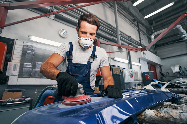 Personne ponçant la carrosserie bleue d'une voiture